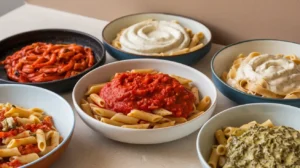 dishes of penne pasta on the same table, each served with a different sauce: Marinara, Arrabbiata, Alfredo, Creamy Garlic, and Pesto.